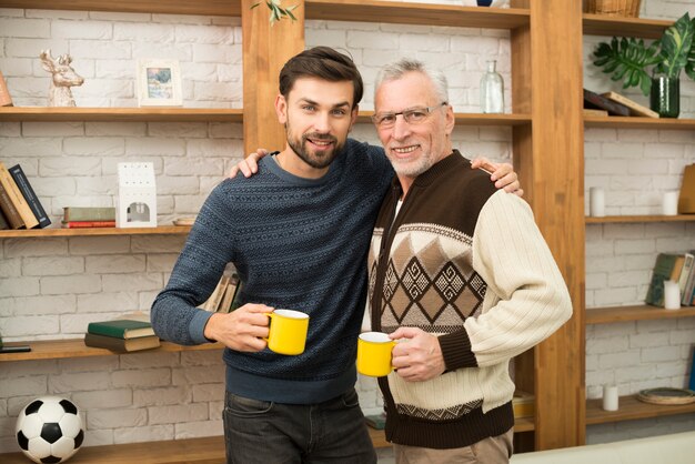 Envelhecido, homem feliz, abraçando, com, sujeito jovem, com, copos, perto, bookshelves