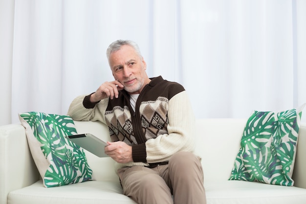 Envelhecido homem pensativo usando tablet no sofá