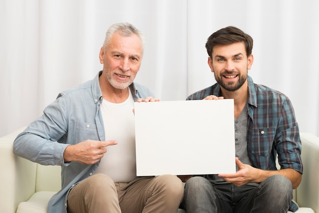 Foto grátis envelhecido, homem sorridente, apontar, papel, e, jovem, feliz, sujeito, ligado, sofá