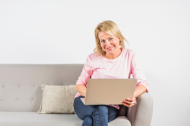 Envelhecido, mulher sorridente, em, rosa, blusa, com, laptop, ligado, sofá