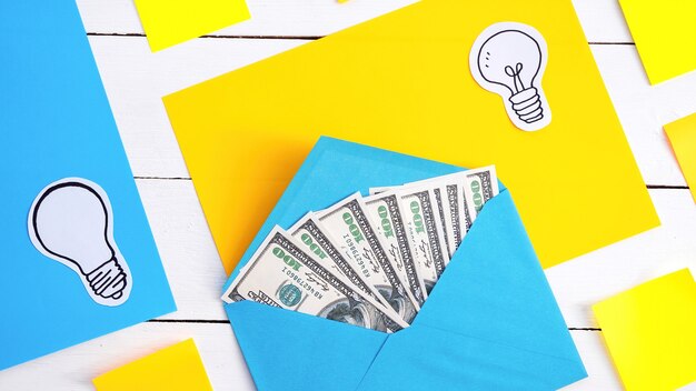 Envelope azul com dinheiro com papéis amarelos e azuis, ícones de lâmpada