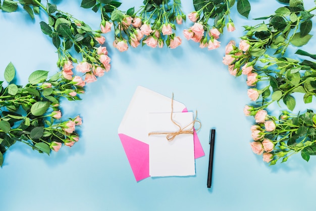 Foto grátis envelope rosa; cartão; caneta e rosas decoração de flores sobre fundo azul