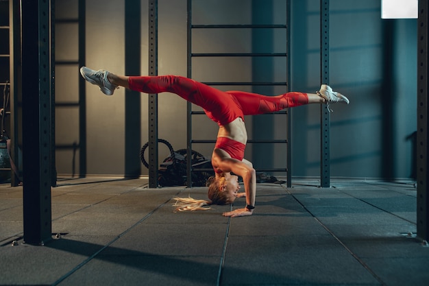 Equilibrado. Jovem mulher caucasiana muscular praticando no ginásio. Modelo feminino atlético fazendo exercícios de força, treinando sua parte inferior, parte superior do corpo, alongamento. Bem-estar, estilo de vida saudável, musculação.