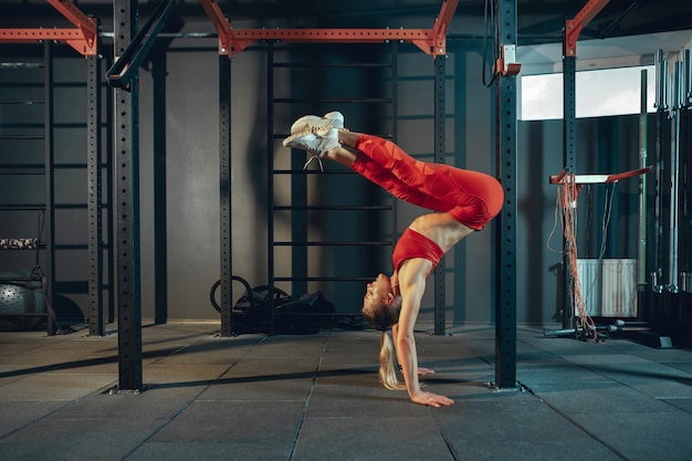 Equilibrado. Jovem mulher caucasiana muscular praticando no ginásio. Modelo feminino atlético fazendo exercícios de força, treinando sua parte inferior, parte superior do corpo, alongamento. Bem-estar, estilo de vida saudável, musculação.