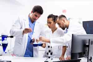 Foto grátis equipe de cientista de jaleco branco trabalhando em conjunto com o fumo de um líquido azul no moderno laboratório de pesquisa.