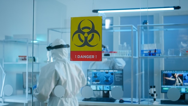 Equipe de cientistas em traje de proteção preparando ferramentas para analisar o desenvolvimento de vírus na zona de perigo do laboratório