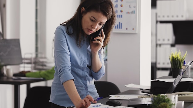 Foto grátis equipe de diversas mulheres analisando papéis no escritório, gerente atendendo telefonema para discutir sobre o relatório de negócios. funcionários colaborando com análises no espaço de coworking. tiro portátil.