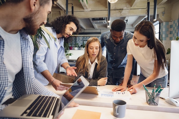 Equipe de diversos colegas de trabalho em um escritório moderno discute seu projeto juntos