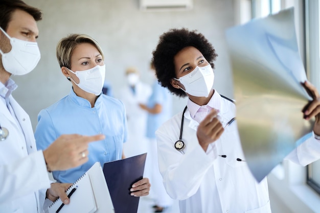 Equipe de médicos com máscaras faciais analisando imagem de raio-x na clínica médica