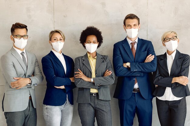Equipe de negócios confiante usando máscaras protetoras em pé com os braços cruzados contra a parede