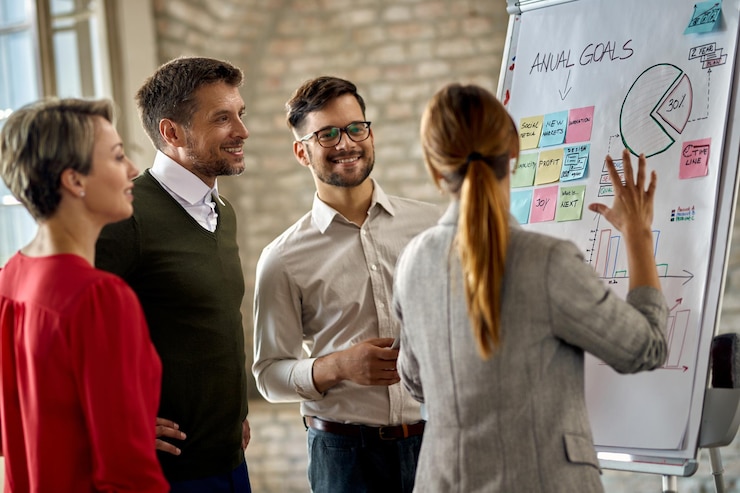 Foto grátis equipe de negócios feliz cooperando enquanto analisa o progresso de seus negócios no quadro branco no escritório