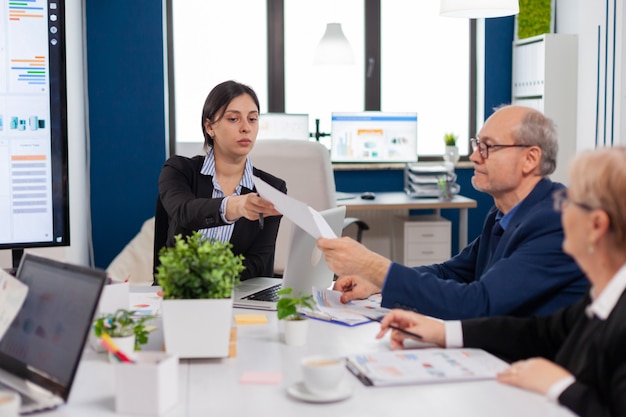 Equipe de negócios multiétnica sentada à mesa no centro do escritório falando sobre o projeto durante a reunião em sala ampla