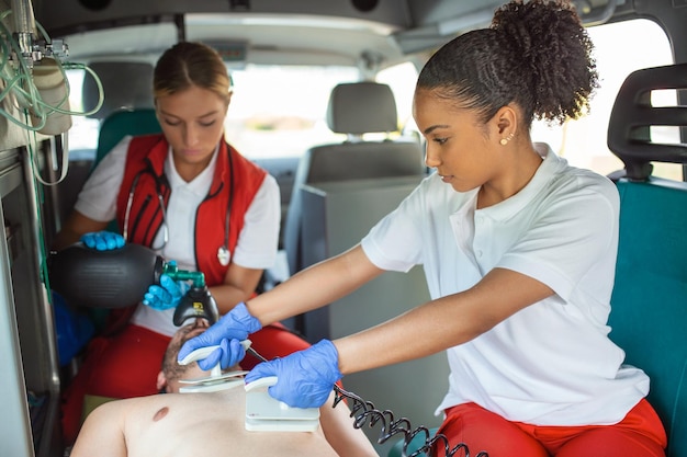 Foto grátis equipe de paramédicos do ems fornece ajuda médica ao paciente ferido a caminho do hospital assistentes de atendimento de emergência usando um desfibrilador e máscara de ventilação para trazer o homem de volta à vida em uma ambulância