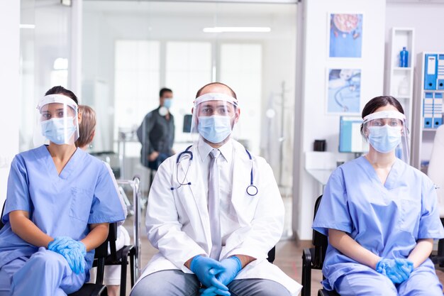 Equipe médica na área de espera da clínica usando máscara facial de proteção contra surto de coronavírus como medida de segurança