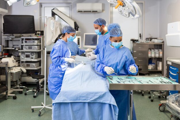 Equipe médica realizando operação Grupo de cirurgião no trabalho na sala de cirurgia em tons de azul Operação médica na sala de operação no conceito de hospital para publicidade de seguros