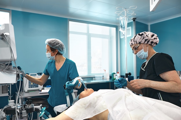 Equipes de um médico em uma moderna sala de cirurgia, conecta o paciente a um dispositivo de ventilação pulmonar artificial, os anestesiologistas preparam o paciente para a cirurgia pulmonar.