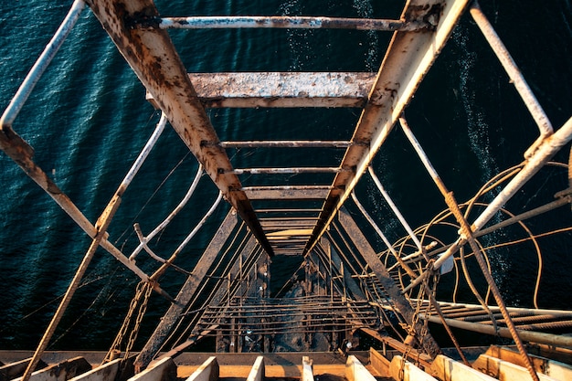 Escada extremamente velha e rasgada, descendo para o mar ondulado a partir de uma ponte velha