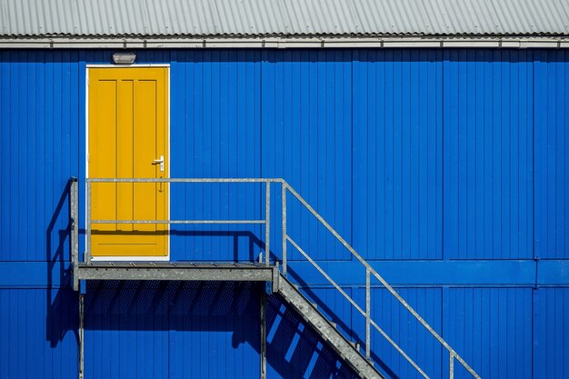 Escada perto da parede azul de uma garagem que leva à porta amarela