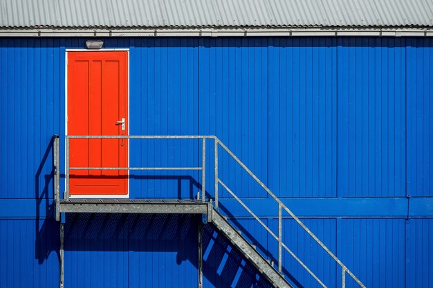 Escada perto da parede azul de uma garagem que leva à porta vermelha