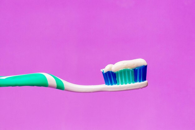 Escova de dentes com creme dental em um fundo roxo, atendimento odontológico