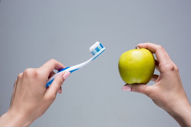 Escova de dentes e maçã nas mãos da mulher em cinza