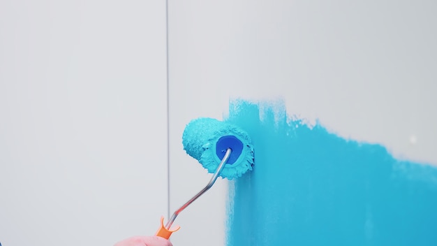 Escova de rolo na parede com tinta azul. Redecoração de apartamento e construção de casa durante a reforma e melhoria. Reparação e decoração.