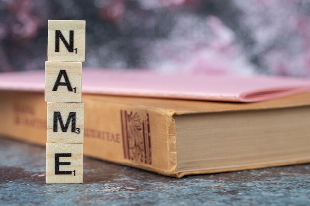 Escrita de nomes com letras pretas em dados de madeira com um livro antigo por perto. Foto de alta qualidade