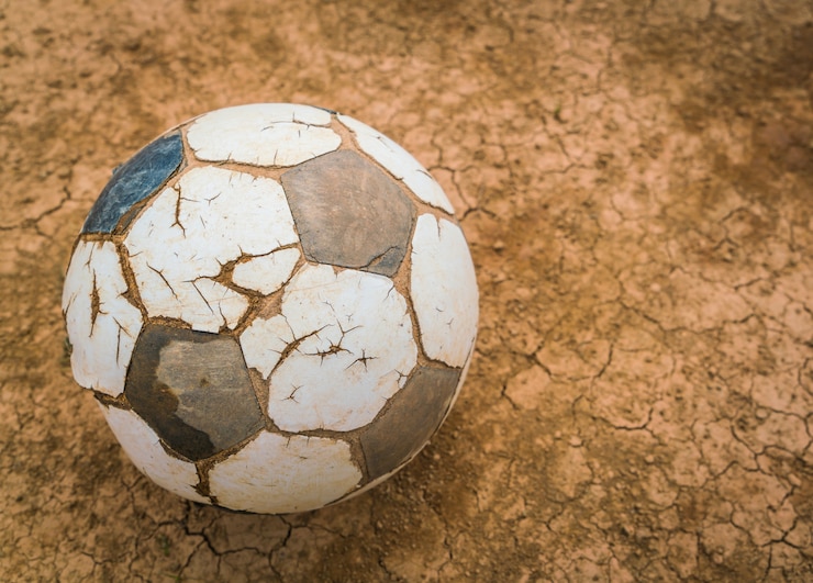 Foto grátis esfera de futebol velha em seco e textura terra rachada.