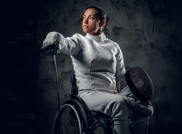 Esgrimista feminina em cadeira de rodas com máscara de segurança de um rosto segurando florete, efeito de poeira na imagem.