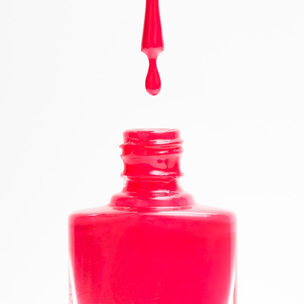 Esmalte vermelho caindo em seu frasco contra um fundo branco