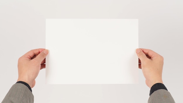 Espaço para texto. a mão está vestindo um terno cinza e segurando papel a4 placa em branco sobre fundo branco.