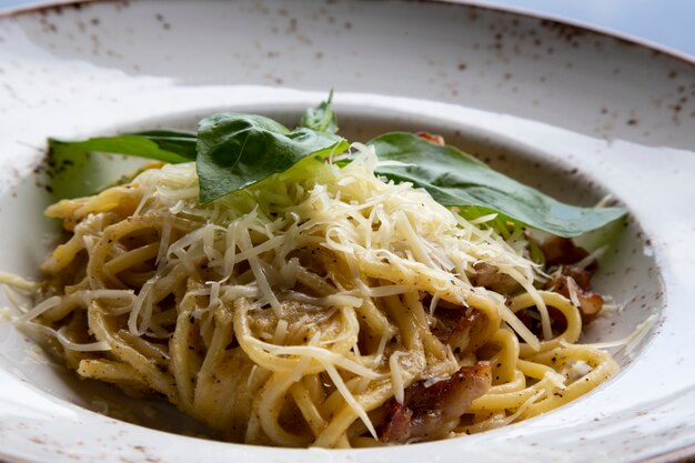Espaguete à carbonara em um prato branco sobre a mesa de um restaurante macarrão de trigo duro com queijo de bacon ... Foto Premium