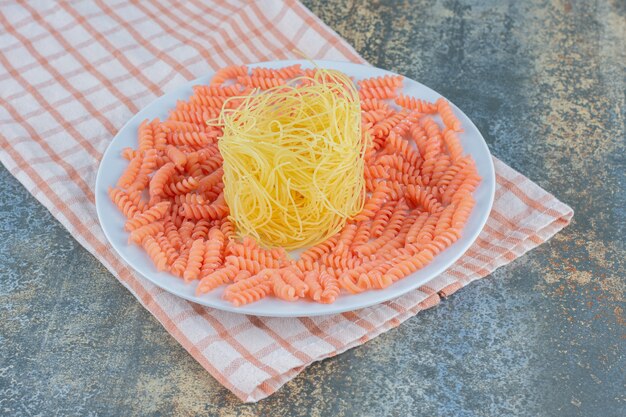 Espaguete cru e macarrão fusilli em tigela sobre toalha, sobre a superfície de mármore.