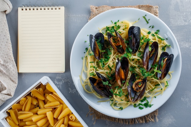 Espaguete e mexilhão em um prato com caderno, macarrão cru, toalha de cozinha