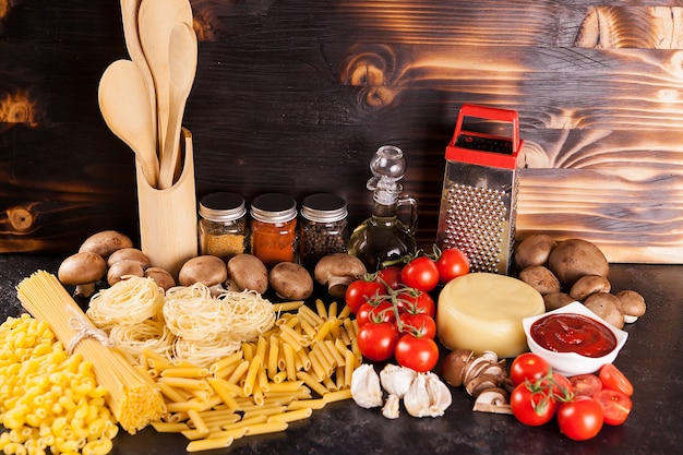 Espaguete, macarrão e macarrão cru ao lado de uma variedade de vegetais frescos e temperos