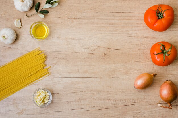 Esparguete não cozinhado; óleo; alho; cebola e tomate vermelho na mesa de madeira com espaço de cópia para escrever o texto