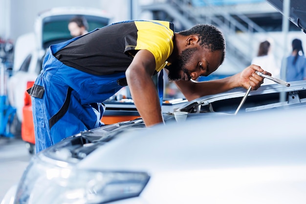 Especialista BIPOC em serviço de automóveis usando ferramentas mecânicas profissionais para reparar o sistema de ignição quebrado Especialista licenciado em garagem de reparação de automóveis de clientes garantindo o desempenho automotivo ideal