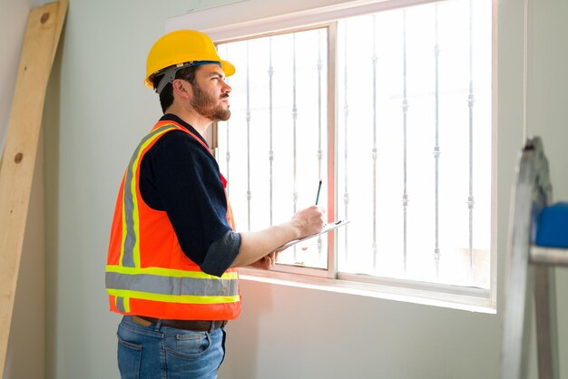 Especialista de inspeção focado com um capacete de segurança verificando a qualidade das janelas e paredes no canteiro de obras