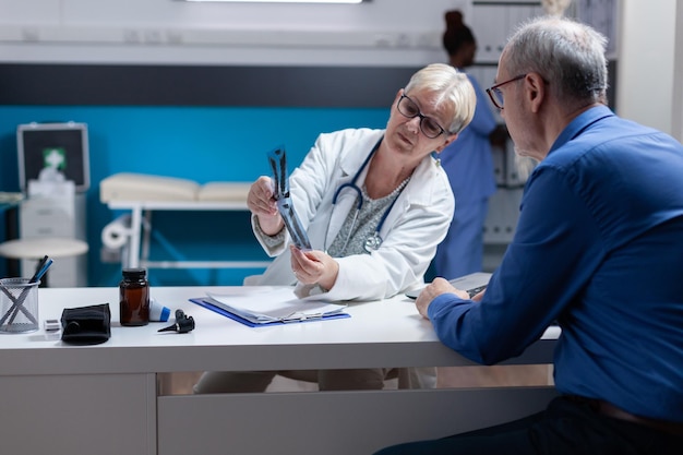 Especialista que explica o diagnóstico de radiografia ao paciente com doença na consulta médica. Médico de saúde mostrando resultados de exames de raio-x a um homem doente na visita de check-up anual.