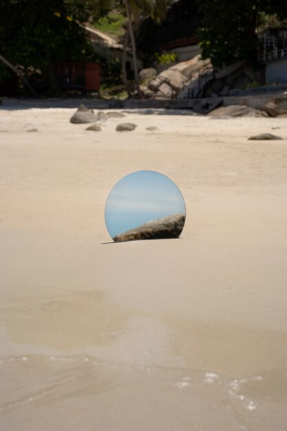 Espelho de vidro redondo na praia refletindo a paisagem