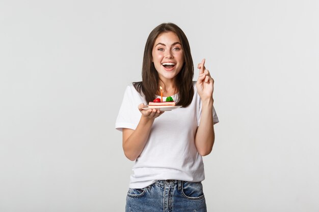 Esperançosa e feliz e sorridente aniversariante cruzar os dedos e fazer o desejo ao soprar uma vela no bolo de aniversário.