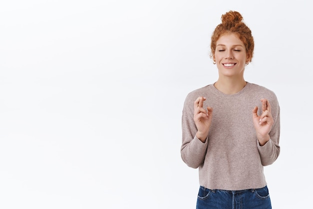 Foto grátis esperançosa mulher ruiva linda com cabelo encaracolado no coque fecha os olhos e sorrindo feliz sonha com os dedos cruzados boa sorte espero que algo aconteça acredite que sonhos se tornem realidade faça desejo