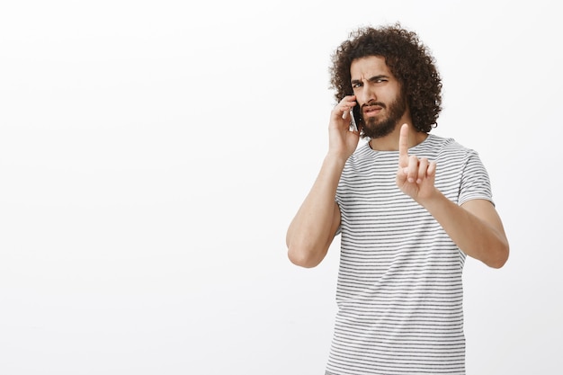 Foto grátis espere um pouco, é uma chamada importante. homem atraente masculino mandão com barba e penteado afro, mostrando o dedo indicador em um gesto de silêncio ou espera