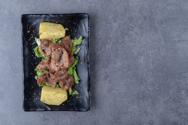 Espetada de carne e batatas cozidas na placa preta.