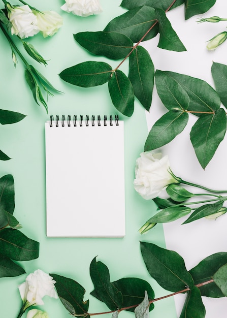 Foto grátis espiral notepad eustoma flores e folhas em fundo verde e branco dual