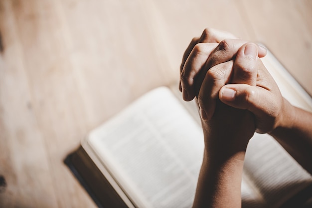 Espiritualidade e religião, as mãos postas em oração sobre uma Bíblia Sagrada na igreja conceito de fé.