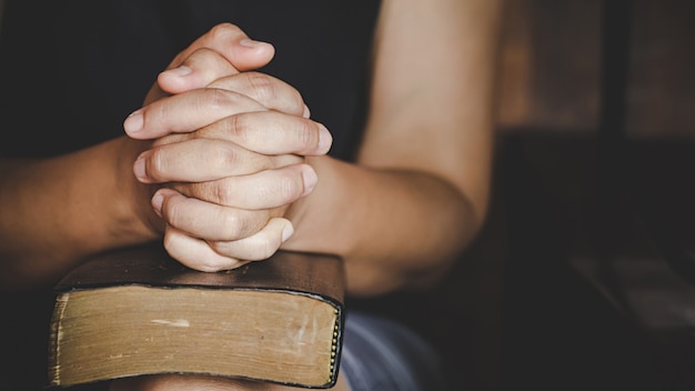 Espiritualidade e religião, as mãos postas em oração sobre uma Bíblia Sagrada na igreja
