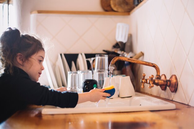 Esponja de lavar roupa linda garota na pia da cozinha