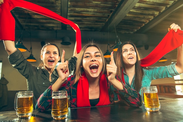 Esporte, pessoas, lazer, amizade, conceito de entretenimento - fãs de futebol feminino felizes ou bons jovens amigos bebendo cerveja, comemorando a vitória em um bar ou pub. Conceito de emoções positivas humanas