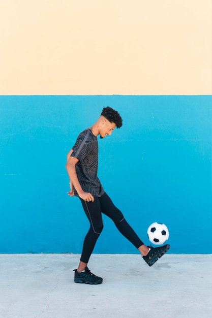 Esportista alegre chutando a bola de futebol perto da parede